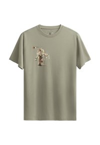 T-shirt in cotone verde oliva con stampa grafica sul petto, caratterizzata da motivi geometrici e un'illustrazione di figura stilizzata.