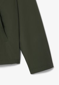 Giacca impermeabile verde con una texture liscia e opaca, maniche lunghe e dettagli con tasche laterali. Design semplice senza hardware visibile.