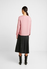 Maglietta a maniche lunghe rosa abbinata a una gonna plissettata nera. La maglietta ha un collo rotondo e polsini elasticizzati; la gonna arriva sotto il ginocchio.