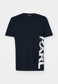 Svart bomulls-t-shirt med rund hals och korta ärmar, med "KARL" tryckt i stora vita bokstäver på vänster sida.