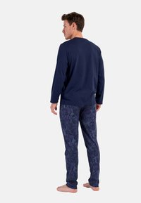 Marines-hemden mit langen Ärmeln, kombiniert mit gemusterten lila Hosen, die ein Blumenmuster aufweisen. Weicher, leichter Stoff mit lockerer Passform.