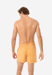 Pantaloni da bagno arancioni con vita elasticizzata, tasche laterali e una vestibilità rilassata, mostrati su un modello maschile di spalle.