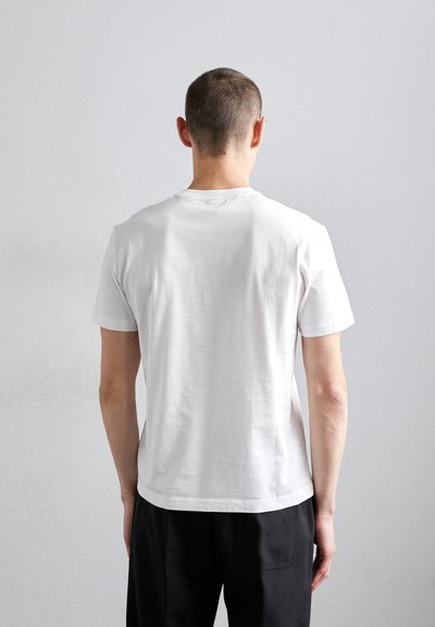 Camiseta blanca de algodón con cuello redondo, mangas cortas y un corte relajado. La parte posterior es lisa con detalles de costura en el cuello.