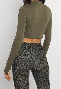 Olivengrünes langärmliges Crop-Top kombiniert mit enganliegenden Leggings im schwarzen und grauen Leopardenmuster, aus einem weichen, elastischen Material mit einem eleganten Design.