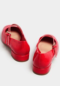 Punaiset kiiltävät nahkakengät, joissa on pyöristetty kärki, matala lohkareseppä ja ohut nilkkastrappi, jossa on metallinen solkiyksityiskohta.