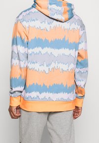 Hoodie med pastellfärgade vågor i orange, blått och grått. Tillverkad av mjukt material, med en känguruficka och ribbade ärmslut.