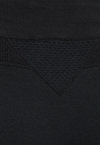 Primo piano di tessuto nero strutturato che mostra un motivo a maglia triangolare con sezioni tessili rigate e lisce variabili.