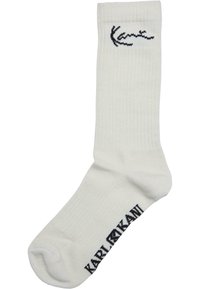 Weiße Baumwollsocke mit gerippter Textur, versehen mit einem schwarzen, nahe dem oberen Rand gestickten "Kani"-Logo. Standard Crew-Längenstil.