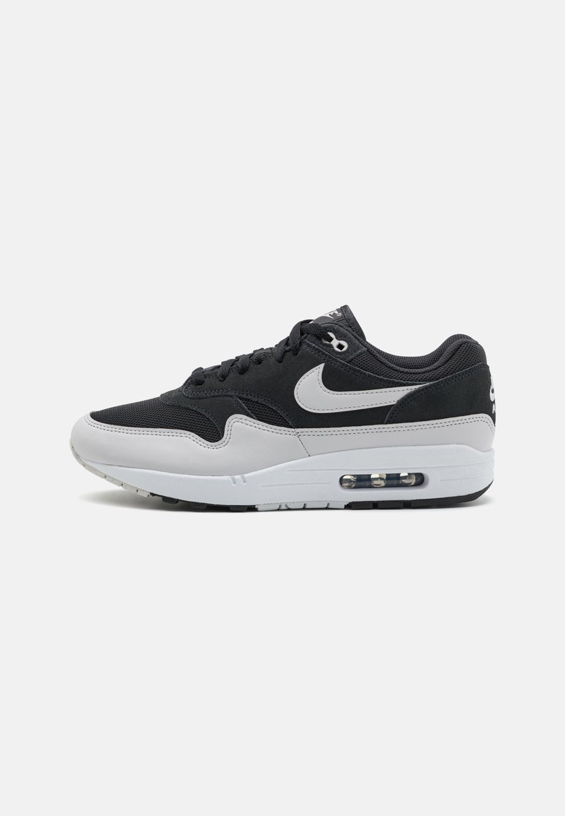 Tenis preto e cinza com parte superior em malha, detalhes em couro, amortecimento Air visível na sola, e uma entressola branca com sola preta.