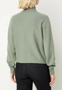 Maglione a coste di colore verde chiaro con colletto alto e maniche leggermente a sbuffo, indossato sopra jeans scuri. Mostra la vista posteriore.