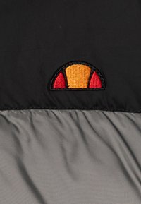 Black fabric featuring a diagonal gray section. An embroidered logo in orange and red appears at the top, resembling a semi-circle with accents.