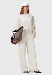 Sudadera crema y pantalones de pierna ancha hechos de un material suave, combinados con un bolso marrón texturizado y bailarinas con estampado. Accesorio de gorro blanco.