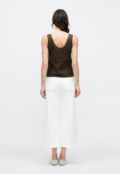 Καφέ λινό αμάνικο τοπ με στρογγυλή πλάτη και λευκό παντελόνι με φαρδιά παντελόνια. Το σύνολο χαρακτηρίζεται από μινιμαλιστικό σχεδιασμό και άνετη εφαρμογή.