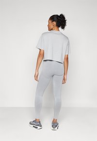 Camiseta corta de color gris claro con mangas cortas, combinada con leggings grises y zapatillas deportivas grises, con un diseño texturizado.