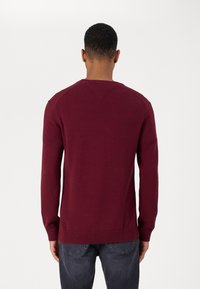 Pull en tricot bordeaux avec des manches longues, un ourlet côtelé et des détails de couture aux épaules. Texture douce, coupe ajustée et sans motifs visibles.