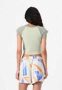 Green cropped t-shirt with short sleeves, paired with colorful, patterned shorts featuring abstract shapes in blue, orange, and green.