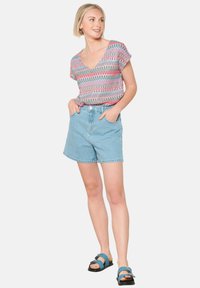 Korte mouwen, V-hals top met een veelkleurig geometrisch patroon, gecombineerd met lichtblauwe denim shorts en teal sandalen met een gespdetail.