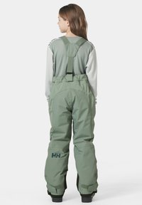 Pantalones de nieve verdes con tirantes ajustables, refuerzo en la parte trasera y detalle del logo en el muslo izquierdo. El material parece duradero y resistente a la intemperie.