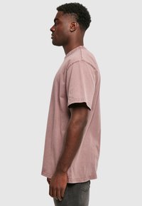 Lühikeste varrukatega, pleekinud roosakas-lilla T-särk, millel on lõdvestatud lõike, nähtavad õmblused ja ümar kaelus. Kantud tumedate teksadega.