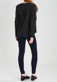 Svart och grått melerat långärmad topp med en avslappnad passform, tillsammans med mörkblå skinny jeans och svarta platta skor.