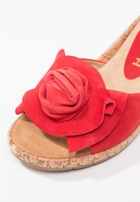 Sandale à bout ouvert avec semelle en liège et dessus en suède rouge, ornée d'un détail décoratif en forme de rose sur la sangle avant.