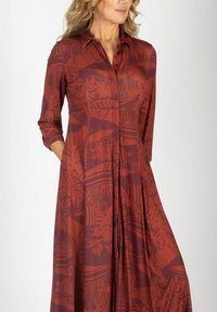 Długa, rdzawego koloru sukienka z kołnierzykiem, rękawami o długości trzech ćwiartek oraz roślinnym wzorem, wykonana z lekkiego materiału i z plisowanym wykończeniem.