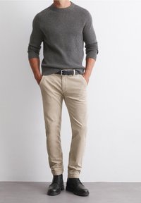 Světlé šedé žebrované svetřík, béžové kalhoty, černý pásek a černé boty na šněrování. Ležérn�í outfit s texturovanými materiály a neutrálními barvami.