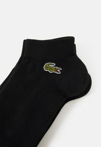 Chaussettes noires à chevilles en matériau doux, avec un poignet côtelé et un logo de crocodile brodé vert sur le côté.