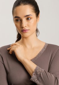 Brun långärmad topp med v-ringning som har en delikat spetskant längs kragen och ärmsluten. Slät textur, figurnära design.