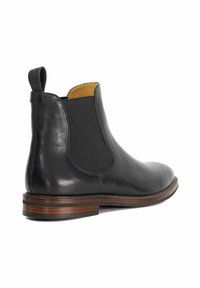 Black leather Chelsea boot with elastic side panels, rounded toe, low stacked heel, and a contrasting brown outsole.