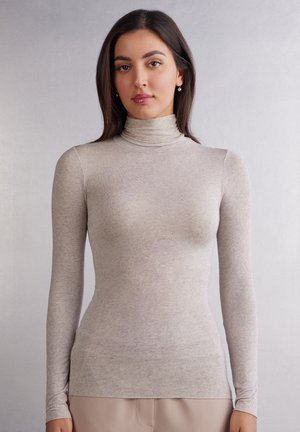 Haut col roulé gris clair en tissu doux et texturé. Il présente des manches longues et une silhouette ajustée, avec une finition lisse et une légère extensibilité.