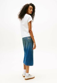 T-shirt blanc à manches courtes associé à une jupe midi en denim, avec des poches arrière et un logo de marque brodé. Des baskets blanches complètent le look.