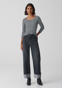 Gestreiftes schwarz-weißes Langarmoberteil, kombiniert mit hoch geschnittenen, dunklen Jeans mit weitem Bein; die Jeans haben hellblaue Denim-Abschlüsse und eine glatte Textur.