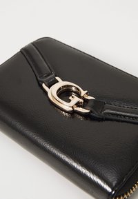 Must black leather rahakott, mis on varustatud kõverate kuldsetest metallist kinnitustega. Tekstuuriga pind, millel on tõmblukk ja stiilne, kompaktne disain.