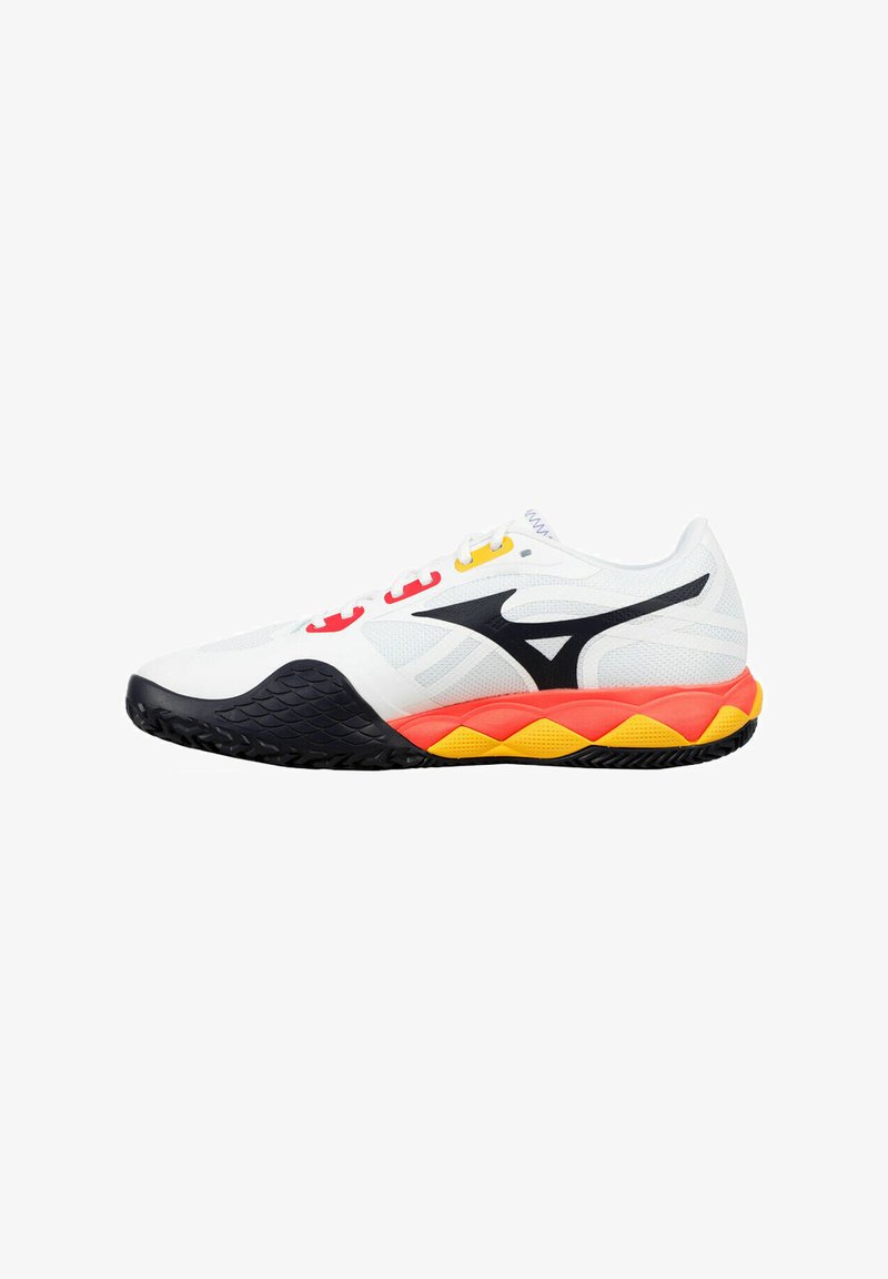 Zapatilla deportiva blanca con parte superior de malla, acentos en negro y una entresuela de goma colorida que presenta secciones en rojo, amarillo y naranja; suela texturizada.