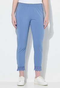 Ljusblå leggings med elastisk midja och spetsdetaljer vid bensluten, tillsammans med vita sneakers på en enhetlig bakgrund.