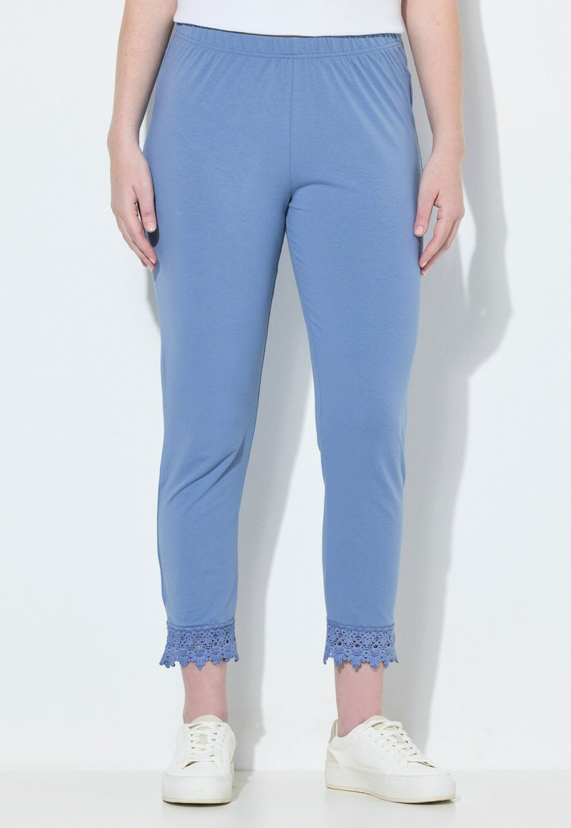 Ljusblå leggings med elastisk midja och spetsdetaljer vid bensluten, tillsammans med vita sneakers på en enhetlig bakgrund.