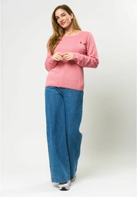 Roze lange mouwen trui met een ronde hals, gecombineerd met brede blauwe spijkerbroek. Schoenen zijn zilver met een chunky zool.