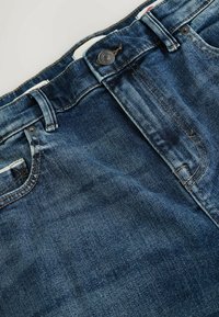 Dżinsy z denimu w ciemnym niebieskim kolorze z przetarciami, pięciokieszeniowy fason, metalowe okucia w pasie oraz detale przeszyć.