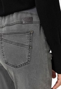 Pantaloni in denim grigio con una tasca posteriore decorata da una stella e un'etichetta nera texturizzata con la scritta "RAPHAELA." Design morbido e aderente.