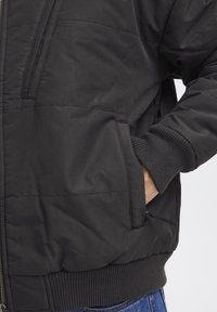 Svart puffjakke med quiltet tekstur, ribbede mansjetter, glidelomme og en avslappet passform. Stoffet ser glatt og litt skinnende ut.