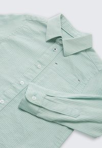 Chemise rayée vert clair à boutons, col pointu, poche poitrine et poignets boutonnés sur une surface plane.