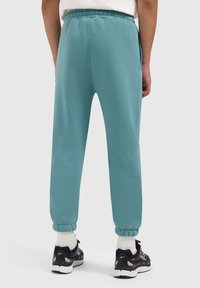 Teal joggingbroek met een trekkoord in de taille, elastische boorden en een zachte textuur, gecombineerd met zwarte sneakers en witte sokken.