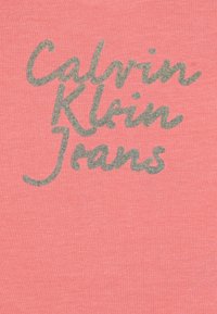 Calvin Klein Jeans logo printed in grey on a coral background. Material appears soft, with a smooth texture and casual design.