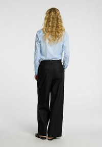 Camicia a maniche lunghe blu chiaro abbinata a pantaloni larghi neri, caratterizzati da una texture del tessuto liscia e un design minimalista.