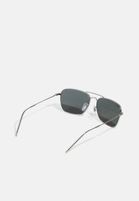 Metal sunglasses with angular, dark gray lenses, featuring thin wire frames and clear nose pads. Sleek and minimalist design.