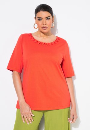 T-shirt rosso a maniche corte con collo texturizzato e arricciato. Tessuto liscio, vestibilità comoda. Abbinato a pantaloni verdi a vita alta con pieghe a gamba larga.