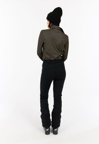Pantalons de ski noirs avec des zips aux chevilles, associés à un haut à col roulé rayé noir et or. Superposés avec un bonnet noir côtelé.
