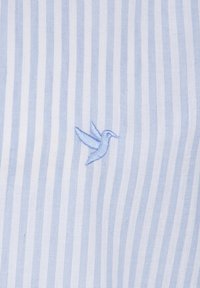 Tejido a rayas en azul claro y blanco que presenta un pequeño colibrí bordado en un azul suave, con una textura lisa y apariencia similar al algodón.