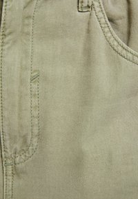 Beige bavlněná tkanina s hladkou strukturou, vybavená boční kapsou a kontrastním prošíváním.